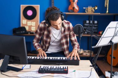 Young hispanic man musician playing piano at music studio