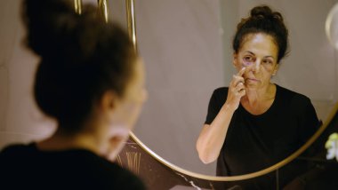 Orta yaşlı İspanyol kadın aile içi şiddet yüzünden acı çekiyor. Banyodaki aynadaki morluklara bakıyor.