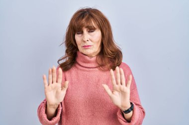 Middle age hispanic woman standing over isolated background moving away hands palms showing refusal and denial with afraid and disgusting expression. stop and forbidden. 