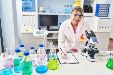 Young hispanic woman wearing scientist uniform analysing urine test tube at laboratory