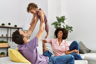 Couple and daughter smiling confident holding child raised up at home
