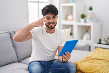 Sakallı İspanyol bir adam kanepeye oturmuş barış sembolü yapıyor. Yüzü parmaklarıyla gülümsüyor ve zafere gülüyor. 