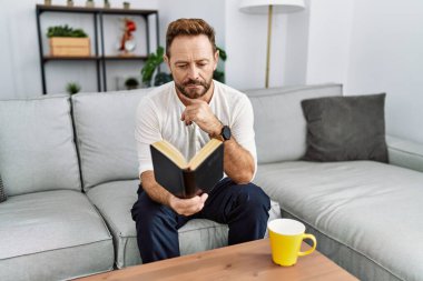 Orta yaşlı İspanyol adam evde kitap okuyor.