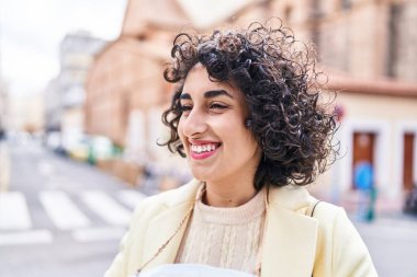 Orta Doğulu genç kadın güler yüzlü, kendinden emin bir şekilde caddenin kenarına bakıyor.