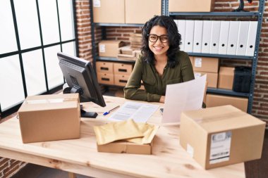 Genç Latin kadın ecommerce iş işçisi ofiste belge okuyor.