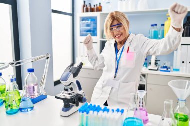 Middle age blonde woman working at scientist laboratory dancing happy and cheerful, smiling moving casual and confident listening to music 