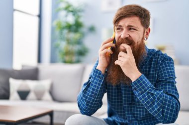 Genç kızıl saçlı adam evde akıllı telefondan konuşuyor diye endişeleniyor.