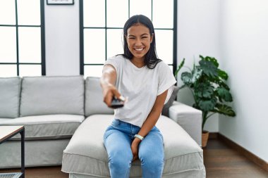 Genç Latin kadın evde televizyon izlerken kendinden emin gülümsüyor.