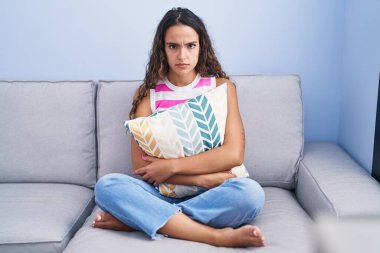 Evdeki koltukta oturan Latin kökenli genç kadın şüpheci ve gergin, sorun yüzünden surat asıyor. negatif kişi. 