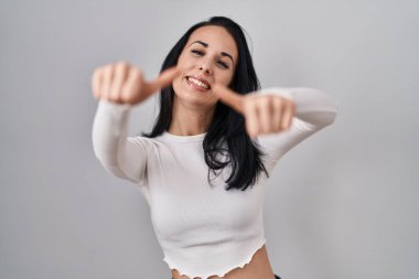 Hispanic woman standing over isolated background approving doing positive gesture with hand, thumbs up smiling and happy for success. winner gesture. 