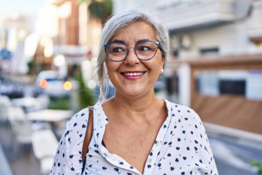 Orta yaşlı bir kadın sokakta kendine güvenerek gülümsüyor.