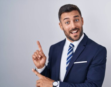 Yakışıklı İspanyol takım elbiseli, kravatlı, gülümseyen ve kameraya bakan iki eli ve parmakları yandan gösteren adam.. 