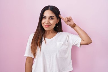 Young arab woman standing over pink background smiling pointing to head with one finger, great idea or thought, good memory 