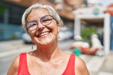 Orta yaşlı, kır saçlı, gülümseyen, kendine güvenen bir kadın.