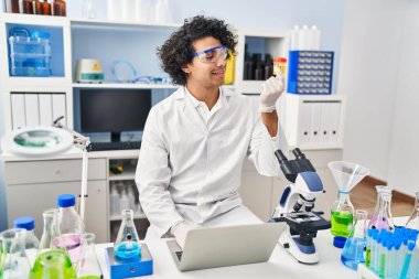 Genç İspanyol adam bilim adamı üniforması giyiyor. Laboratuvarda idrar testi tüpünü inceliyor.