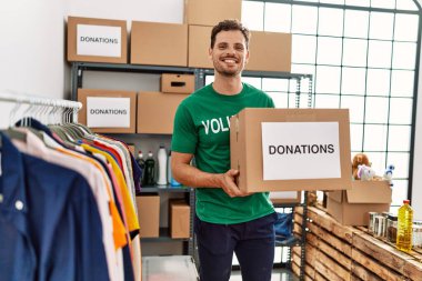 Gönüllü üniformalı genç İspanyol bir adam yardım merkezinde bağış kutusunu tutuyor.