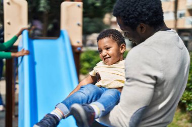 Baba ve oğul oyun alanında kaydırak oynuyorlar.