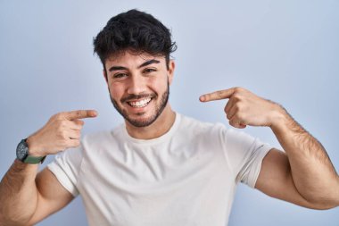 Beyaz arka planda sakallı, neşeli gülümseyen, parmakları ve ağzıyla işaret eden İspanyol bir adam. diş sağlığı kavramı. 