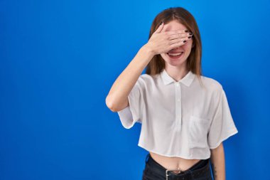 Mavi arka planda dikilen güzel bir kadın. Gülümsüyor ve gülümsüyor. Gözleri şaşkınlıkla örtüyor. kör kavram. 