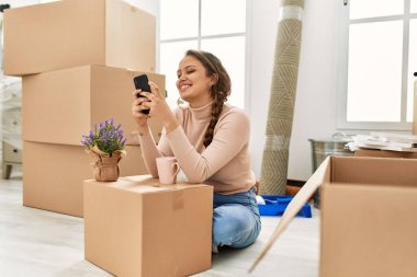 Genç ve güzel İspanyol kadın akıllı telefon kullanıyor. Yeni evinde yerde oturuyor.