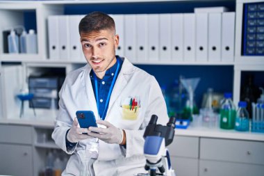 Young hispanic man scientist using smartphone at laboratory