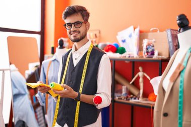 Genç İspanyol terzi gülümsüyor atölyede kumaş ve iplik tutuyor.