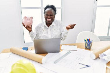 Mimari atölyesinde çalışan Afrikalı genç bir kadın kumbarasında gururla bağırıyor zaferi ve başarıyı kutluyor. 