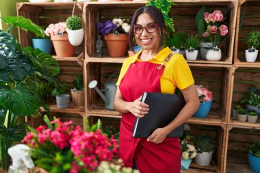 Young beautiful arab woman florist smiling confident holding binder at flower shop