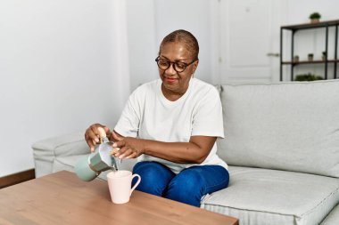 Kıdemli Afro-Amerikan kadın gülümsüyor. Evdeki fincana kendinden emin kahve koyuyor.