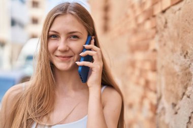 Beyaz bir kadın gülümsüyor ve caddede akıllı telefondan konuşuyor.