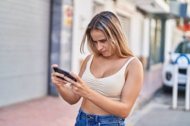 Young blonde woman splaying video game with concentrate expression at street