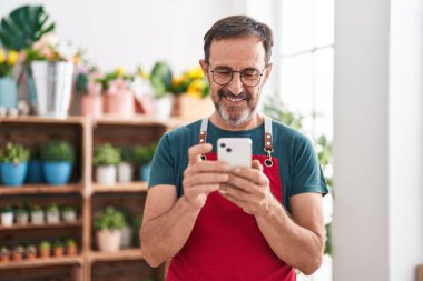 Çiçekçiye akıllı telefon kullanarak gülümseyen orta yaşlı bir çiçekçi.