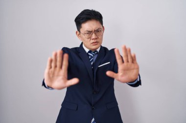 Young asian man wearing business suit and tie doing stop gesture with hands palms, angry and frustration expression 