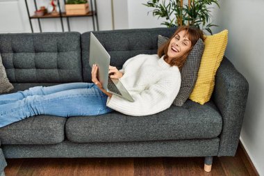 Genç beyaz kadın evdeki kanepede dizüstü bilgisayar kullanıyor.