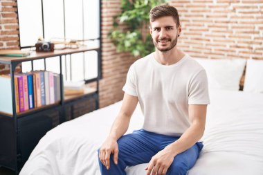 Beyaz bir adam yatakta kendinden emin bir şekilde gülümsüyor.