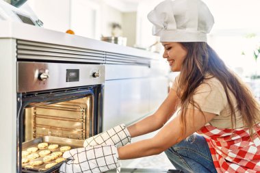 Genç ve güzel İspanyol kadın gülümsüyor. Mutfakta elinde bisküvi tepsisiyle kendine güveniyor.