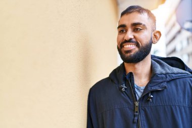 Young hispanic man smiling confident looking to the side at street