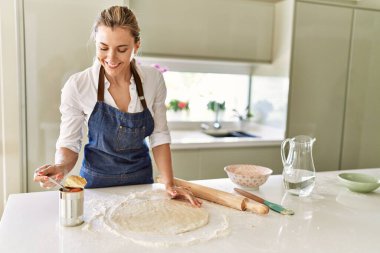 Genç sarışın kadın mutfakta pizza pişirirken kendinden emin gülümsüyor.