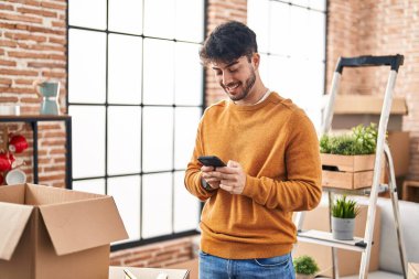 Young hispanic man smiling confident using smartphone at new home