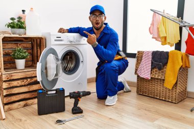 Çamaşır makinesinde çalışan genç Hintli teknisyen parmağını yana doğru göstererek şaşırdı, ağzı açık hayret içinde kaldı.. 