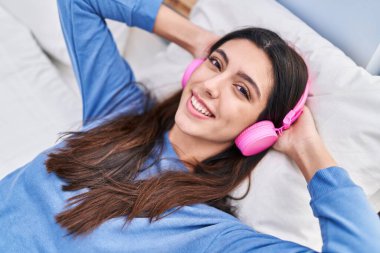 Genç, güzel, İspanyol bir kadın yatakta müzik dinliyor.