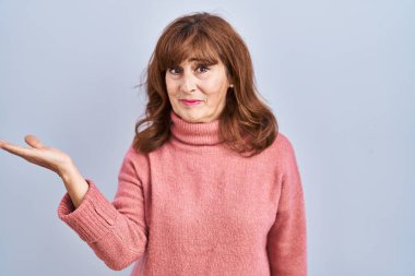 Middle age hispanic woman standing over isolated background smiling cheerful presenting and pointing with palm of hand looking at the camera. 