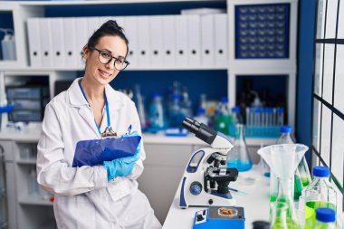 Young caucasian woman scientist weighing pills writing on document at laboratory
