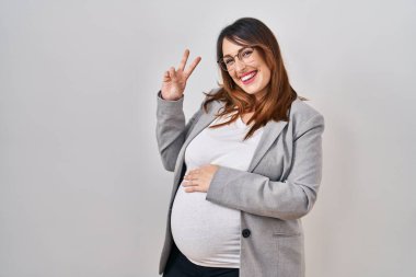 Pregnant business woman standing over white background smiling with happy face winking at the camera doing victory sign. number two. 