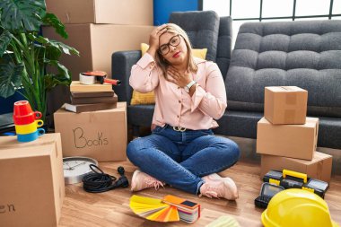 Young hispanic woman moving to a new home sitting on the floor touching forehead for illness and fever, flu and cold, virus sick 