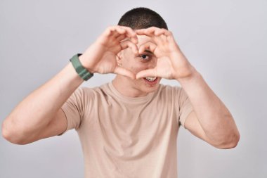 İzole edilmiş arka planda duran genç adam kalp şeklinde elleriyle ve parmaklarıyla tabelanın içinden bakıp gülümsüyor. 