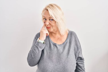 Beyaz arka planda duran orta yaşlı beyaz kadın jestini izlerken gözüne işaret ediyor. Şüpheli bir ifade. 