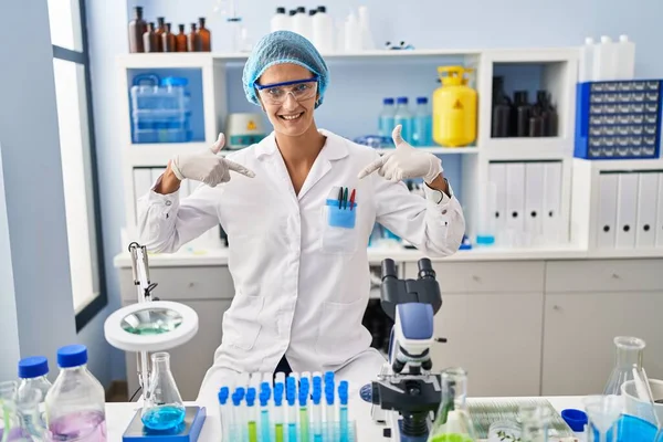 Brunette woman working at scientist laboratory looking confident with smile on face, pointing oneself with fingers proud and happy.