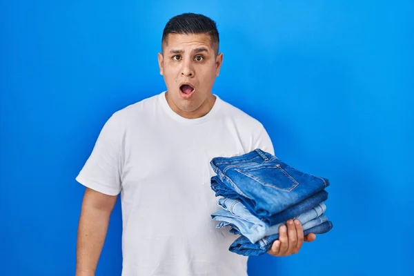Hispanic Young Man Holding Stack Folded Jeans Scared Amazed Open — Stock Photo, Image