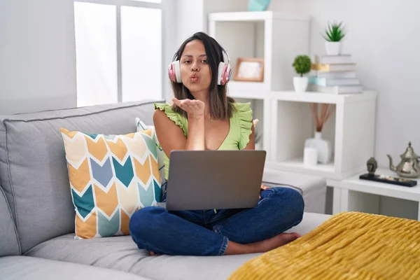 Hispanic young woman using laptop at home looking at the camera blowing a kiss with hand on air being lovely and sexy. love expression.